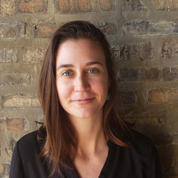 Allison Kanner-Botan in a black shirt in front of a weathered brick wall.