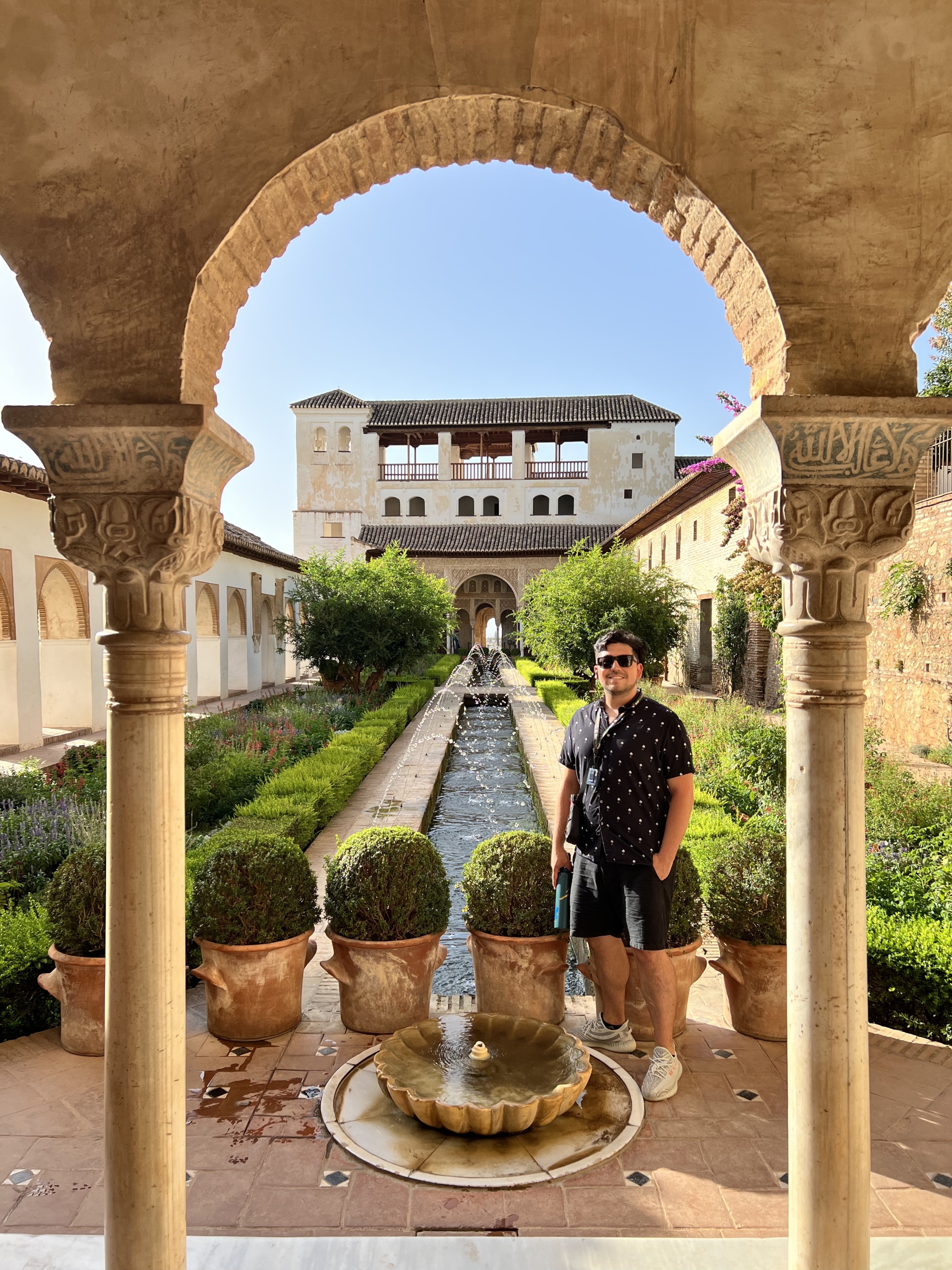 David Montoya standing in a manicured Spanish garden, framed by an arch and pillars.