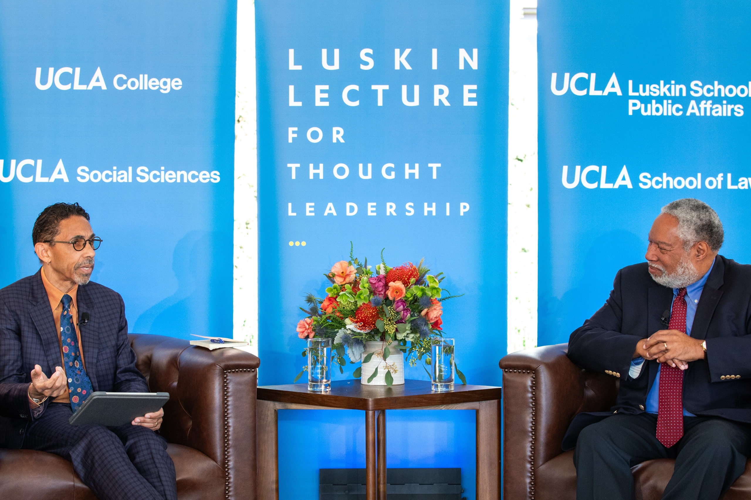 Robin D. G. Kelley and Lonnie G. Bunch III sit in chairs in front of a blue screens that feature the words 