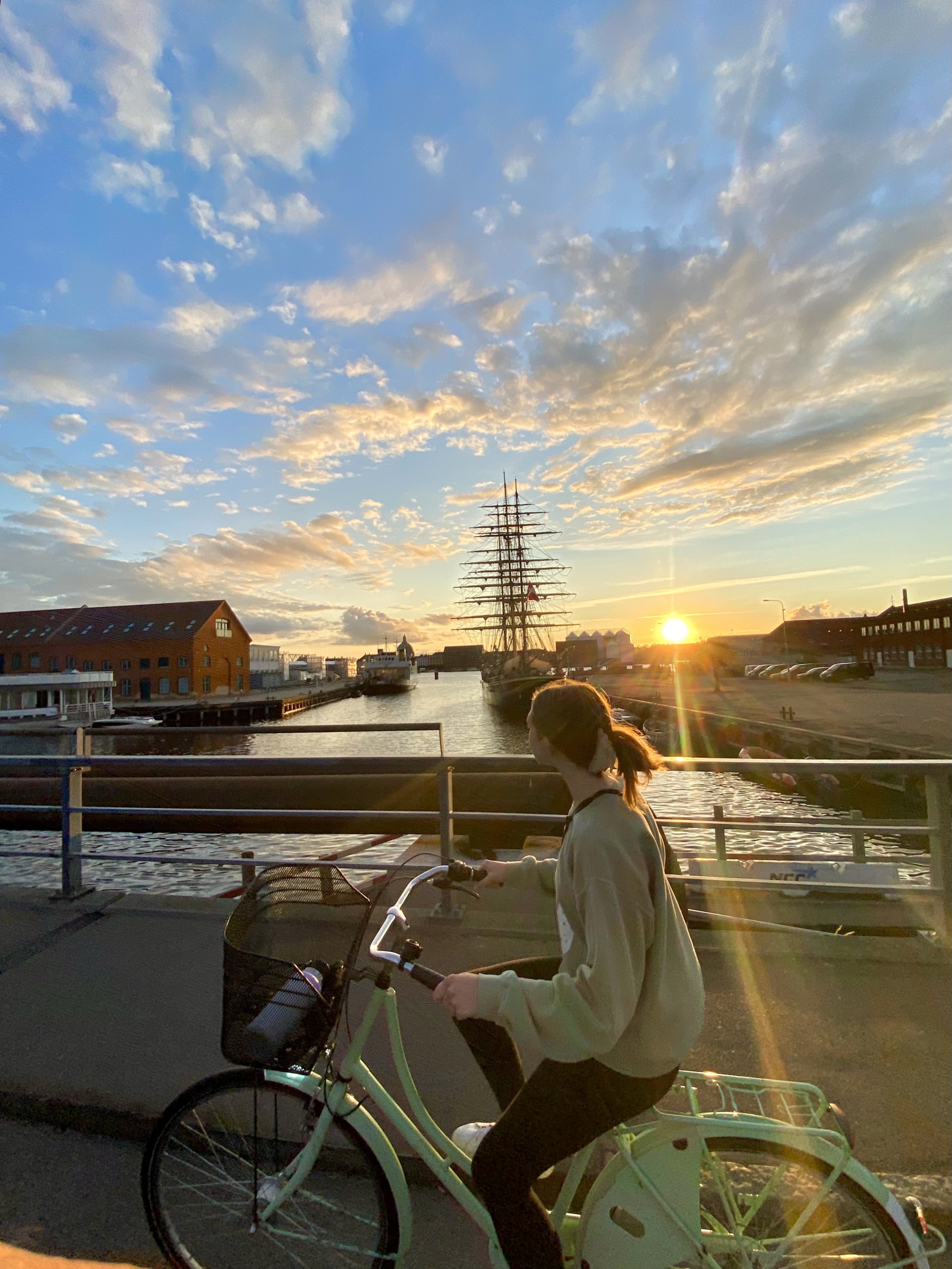 Kendall Vanderwouw riding a bicycle at sunset in Denmark against a cloud-filled sky.