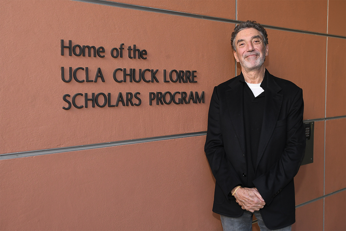 Chuck Lorre in a black jacket with his arms clasped in front of him, standing in from of signage that reads: 