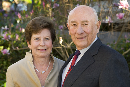 Meyer and Renee Luskin standing outside with the pink flowers of magnolia trees in the background.