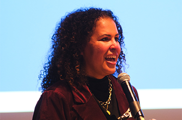 Safiya Noble speaks into a microphone at her installation ceremony as the David O. Sears Presidential Chair in Social Sciences.