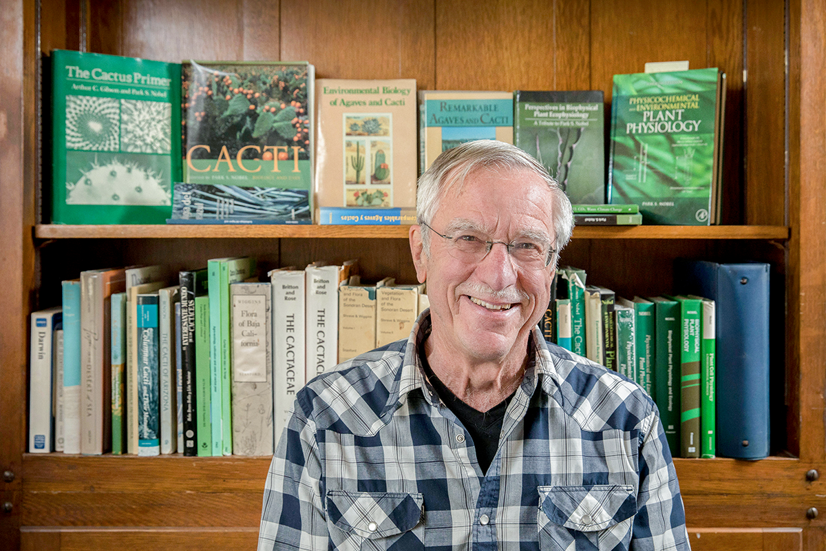 Park Nobel smiling in a blue flannel shirt in front of a bookshelf with books that include a publication of his. 