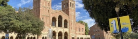 An image of UCLA's Royce Hall, Shapiro Fountain and Dickson Plaza with students sitting in the foreground, under a blue sky with scattered white clouds