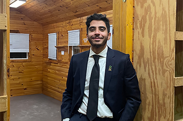 Mohammed Alharthi in suit and tie standing inside a wood-paneled room