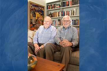 An image of Tom Bye (left) and David Bohne (right) sitting in a room with books and posters superimposed over a blue background.