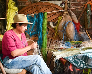 Angelina Sanchez Bustacara in jeans and a pink shirt weaving baskets in Boyacá, Colombia.