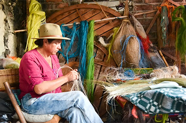 Angelina Sanchez Bustacara in jeans and a pink shirt weaving baskets in Boyacá, Colombia.