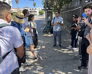 UCLA faculty member Gustavo Leclerc and students speaking on sidewalk near bus stop