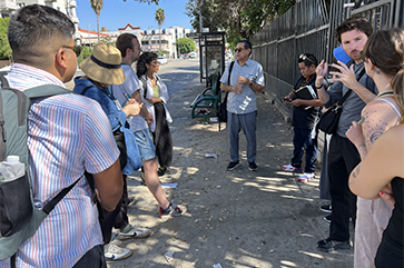 UCLA faculty member Gustavo Leclerc and students speaking on sidewalk near bus stop