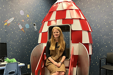 Meg Cychosz sitting in a model rocket ship in her research lab