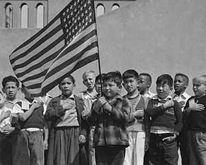 A black and white photograph of multiethinic children saluting the U.S. flag.