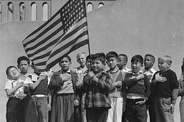 A black and white photograph of multiethinic children saluting the U.S. flag.