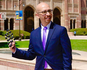 Maher El-Kady holding a molecule diagram as he stands in front of the Shapiro Fountain.