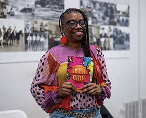 La’Tonya Rease Miles, in colorful top and black-rimmed glasses, holds a copy of her memoir, “Smart Girl: A First-Gen Origin Story.”