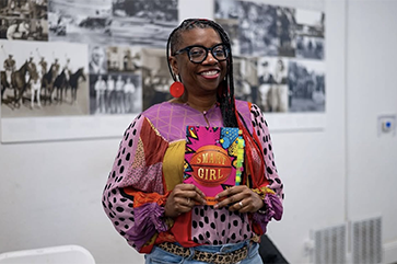 La’Tonya Rease Miles, in colorful top and black-rimmed glasses, holds a copy of her memoir, “Smart Girl: A First-Gen Origin Story.”