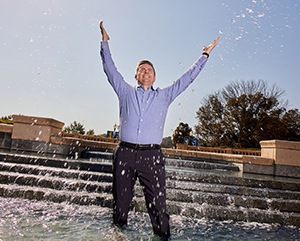 Andrew James-McClure with his hands pointing towards the sky as he dips his feet in UCLA's Shapiro Fountain.