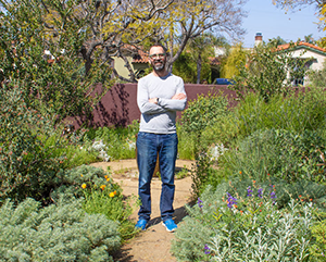 Alex Hall standing in a garden with his arms crossed.