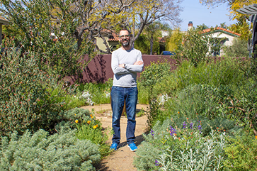 Alex Hall standing in a garden with his arms crossed.