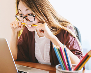 Woman biting pencil as she looks at the computer screen.