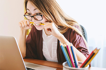 Woman biting pencil as she looks at the computer screen.