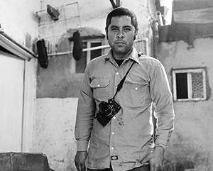 A black and white photograph of Jason De León wearing a camera.
