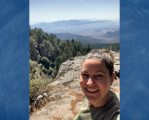 Julie Bernard standing on a mountain lookout point with a mountainous valley in the background.