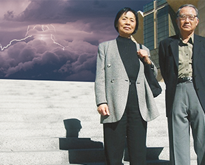 Yoko and Michio Yanai standing at the base of a concrete stairs with clouds and lightning in the background.