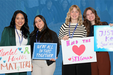 Four women holding signs against a blue background