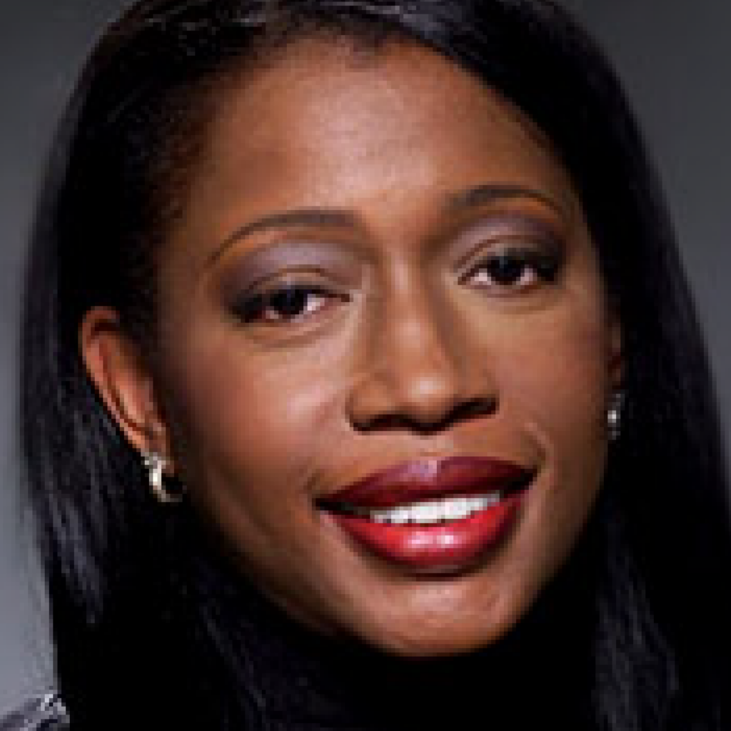 A woman with long straight black hair, wearing small hoop earrings, red lipstick, and subtle eye makeup, smiles in a close-up portrait against a dark background.