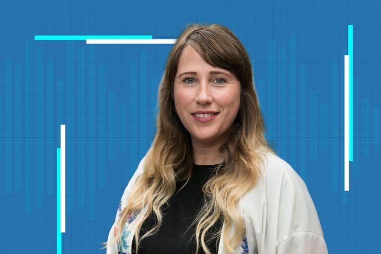 A woman with long, wavy blonde hair and a black top smiles in front of a blue graph-like background with white and blue graphic lines.