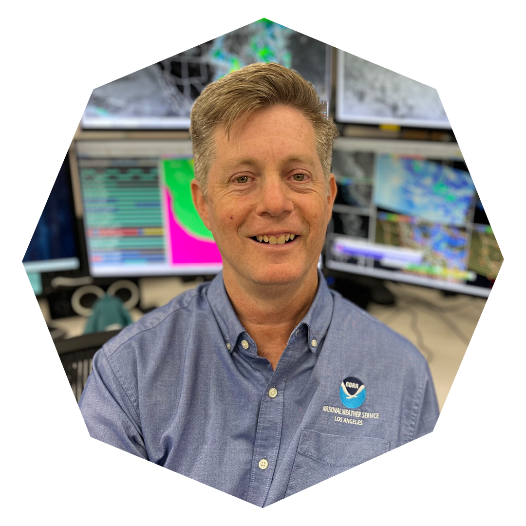 Dave Gomberg in a blue button-up shirt with a National Weather Service logo on it sits in front of various weather maps